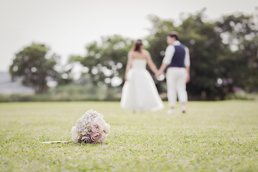 Asian couple wearing wedding costumes relaxed in the park. There is a bouquet on the grass in front.