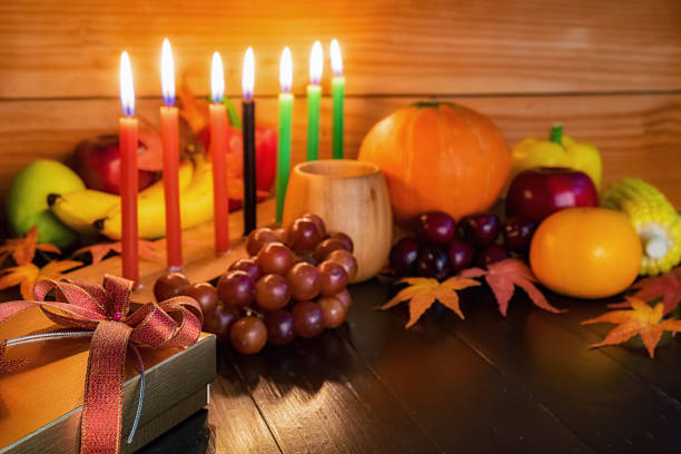 concepto de día de fiesta de kwanzaa con decorar siete velas rojos, negros y verdes, caja de regalo, calabaza, maíz y frutas en el mostrador de madera y fondo. - kwanzaa fotografías e imágenes de stock