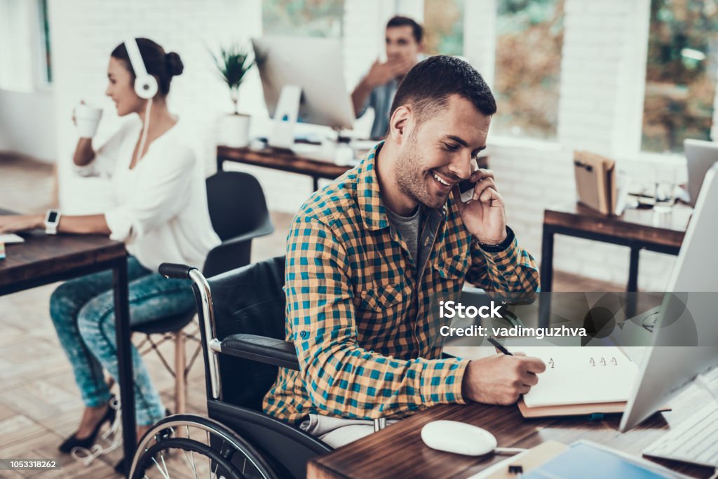 Man on Wheelchair Write Notes and Talking on Phone Man on Wheelchair Write Notes and Talking on Phone. Disabled Young Man. Man on Wheelchair. Recovery and Healthcare Concepts. Teamwork in Office. Young Worker. Sitting Man. Talking on Phone. Disability Stock Photo