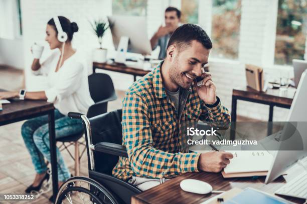 Man On Wheelchair Write Notes And Talking On Phone Stock Photo - Download Image Now - Disability, Working, Wheelchair