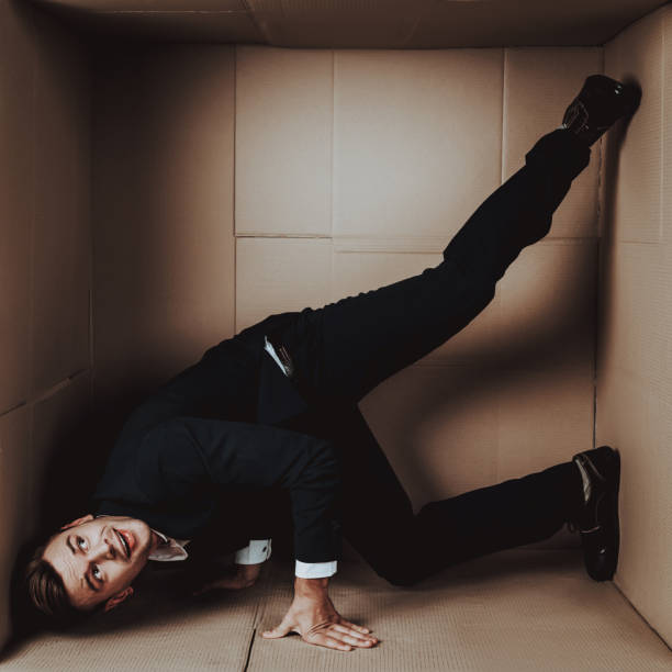 istock Young Businessman in Black Suit in Cardboard Box. 1053320960