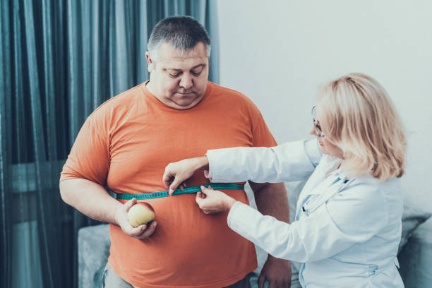 Fat Man with Doctor in White Coat in Gray Room. Fat Man with Doctor in White Coat in Gray Room. Woman with Tailors Centimeter. Diet and Healthcare Concept. Man with Bulimia. Unhealthy Lifestyle Concept. Man with Overweight. Patient with Stomach. centimeter photos stock pictures, royalty-free photos & images
