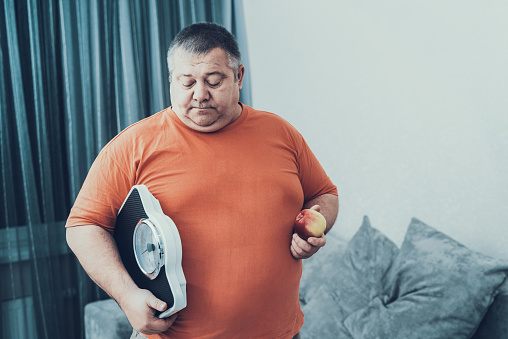 Fat Man i T-shirt with Weighter and Apple in Hands