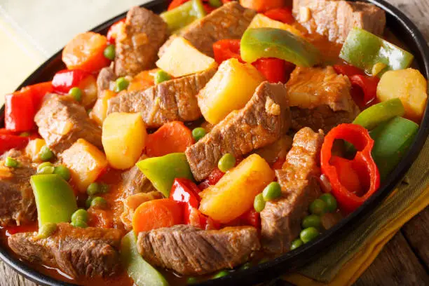 Slow cooked beef with potatoes, peppers, peas, tomatoes and carrots in a spicy sauce close-up on a plate on the table. horizontal