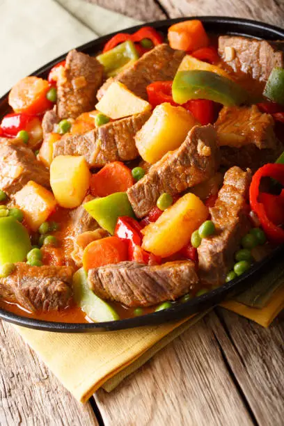 Asian food: Stewed beef with potatoes, peppers, peas, tomatoes and carrots close-up on a plate on the table. vertical