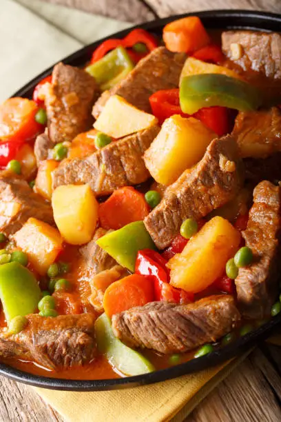 Stew beef with potatoes, peppers, peas, tomatoes and carrots closeup on a plate on the table. vertical