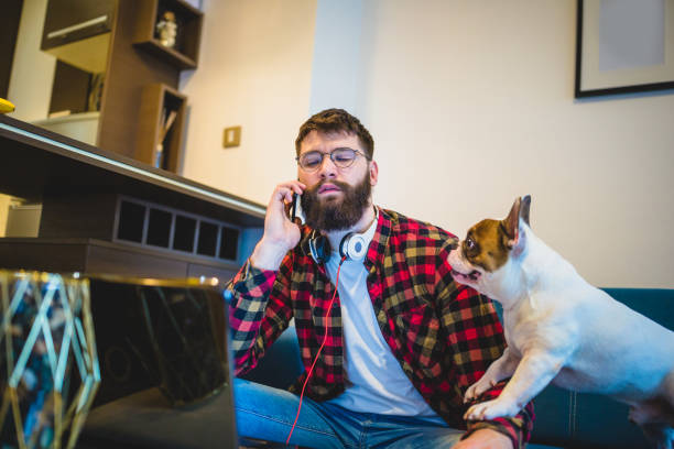 Handsome, hipster man sitting on the living room sofa with his dog, using laptop