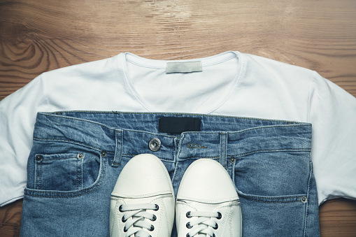 White sneakers jeans and shirt on wooden background.