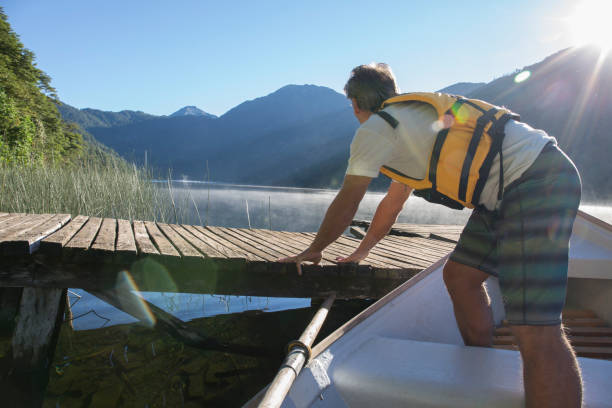 istock Mature man launches rowboat from dock in mountain lake 1053383320