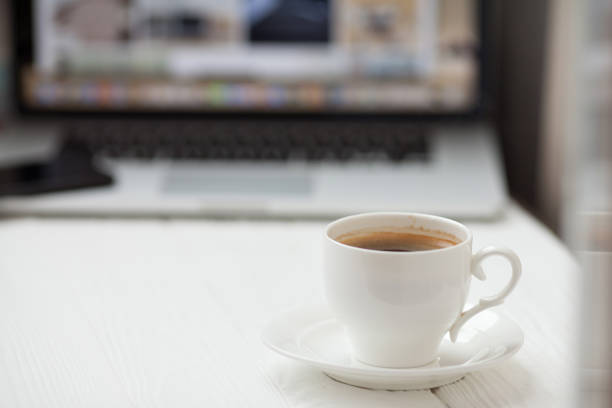 istock Coffee Cup on the white table on blurred laptop background 1053388078