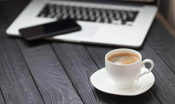 istock Coffee Cup on the black table on blurred laptop background 1053388224