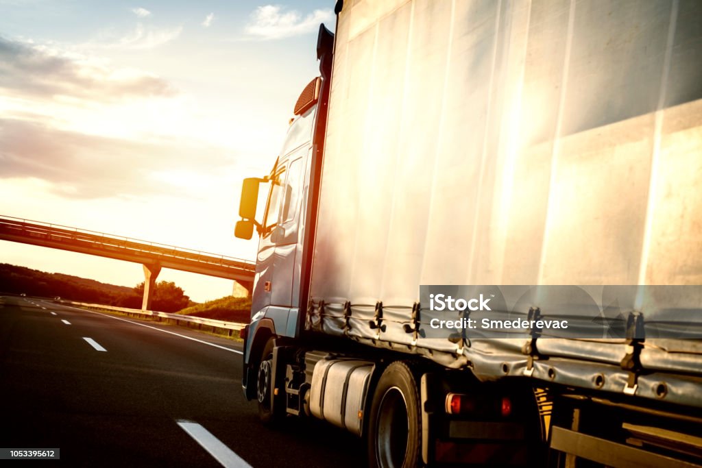 Trucks and freight transportation. Truck on the road in motion. Long vehicle cruising highway in sunset. Truck Stock Photo