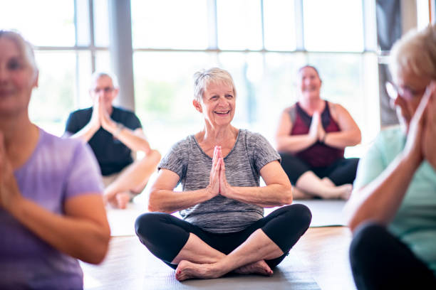 Fun Meditation A group of seniors are sitting crosslegged and meditating in a fitness center. exercise class stock pictures, royalty-free photos & images