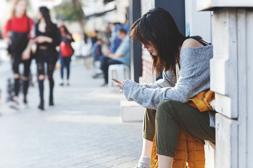 Joven mujer sentada en cerca de la puerta de calle y aplicaciones smartphone photo