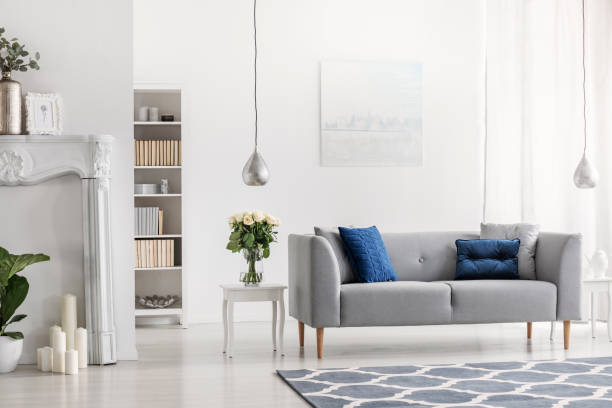 sofá gris con cojines azules en blanco elegante salón interior con flores y pintura. foto real - fireplace living room door wall fotografías e imágenes de stock