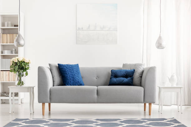 istock Blue pillows on grey couch next to table with flowers in white flat interior with painting. Real photo 1053407138