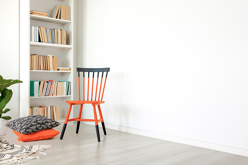 Pillows next to orange and black chair in white room interior with copy space on empty wall. Real photo