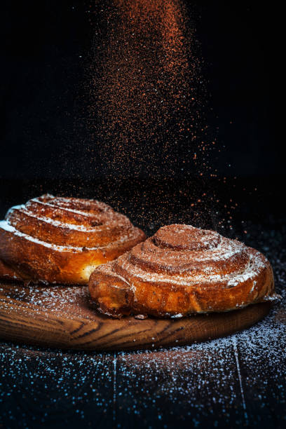 Homemade cinnamon buns with powdered sugar and cacao. Concept of action low key food photography.
