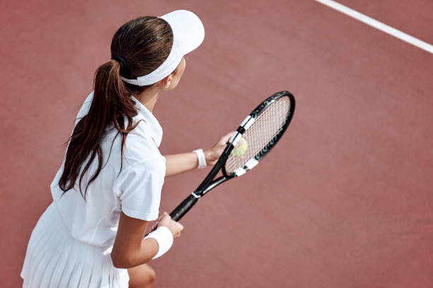 pretty girl plays tennis on the court outdoors. she prepares to beat on a ball. woman wears a light blue sportswear with white sneakers. top view photo. - tennis women one person vitality imagens e fotografias de stock