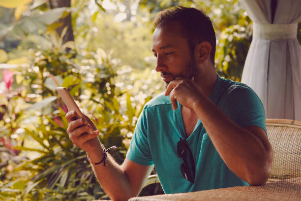 istock Modern man sitting in the tropical garden and using cellphone. 1053425066