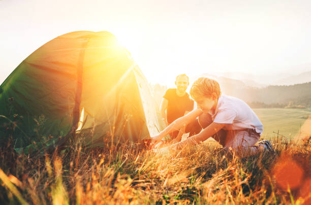 istock Father learn his son set up camping tent on sunset forest glade 1053426506