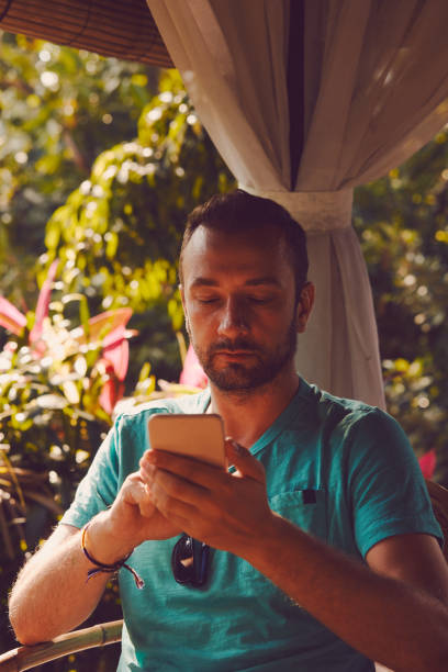 istock Modern man sitting in the tropical garden and using cellphone. 1053426748