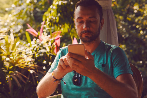 istock Modern man sitting in the tropical garden and using cellphone. 1053426848