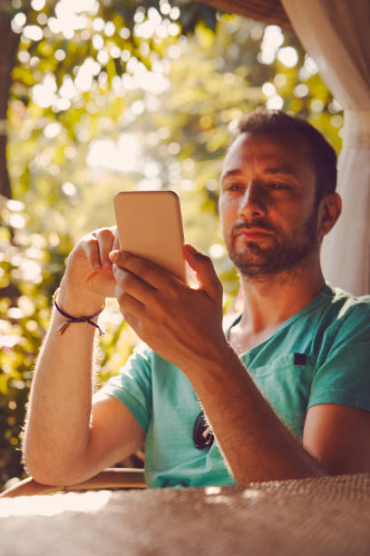 istock Modern man sitting in the tropical garden and using cellphone. 1053427282