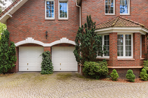 Red brick classic style house with white garage doors and window frames. Cobble in front of the building.