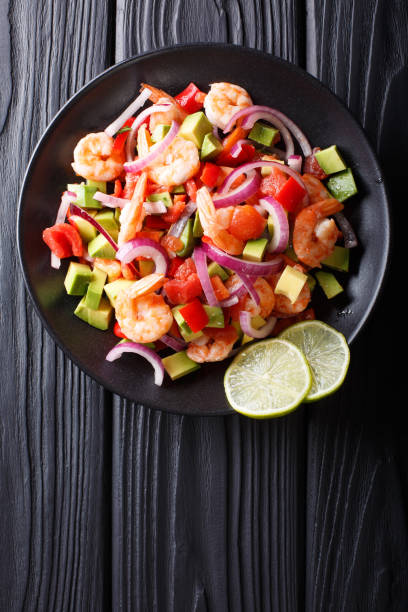 Delicious ceviche of shrimp with vegetables, spices and lime close up on a plate. Vertical top view Delicious ceviche of shrimp with vegetables, spices and lime close up on a plate on the table. Vertical top view from above seviche photos stock pictures, royalty-free photos & images