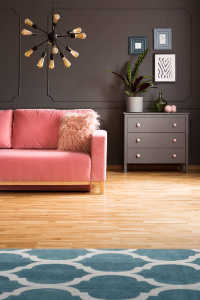 istock Patterned carpet on wooden floor and plant in grey flat interior with pink sofa under lamp. Real photo 1053438952