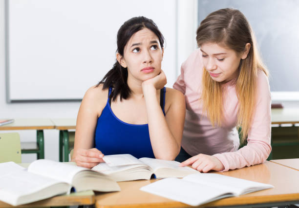 istock Young girl is helping her girlfriend with writing text in the classroom 1053450096