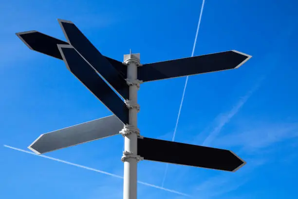 Empty guidepost with arrow shaped labels over blue sky background