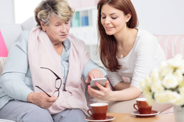istock Smiling daughter showing smartphone to senior woman while drinking tea 1053460566
