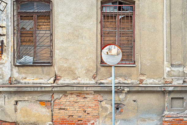 abandoned grunge cracked stucco wall with with boarded up windows. Reflection of building in street mirror.