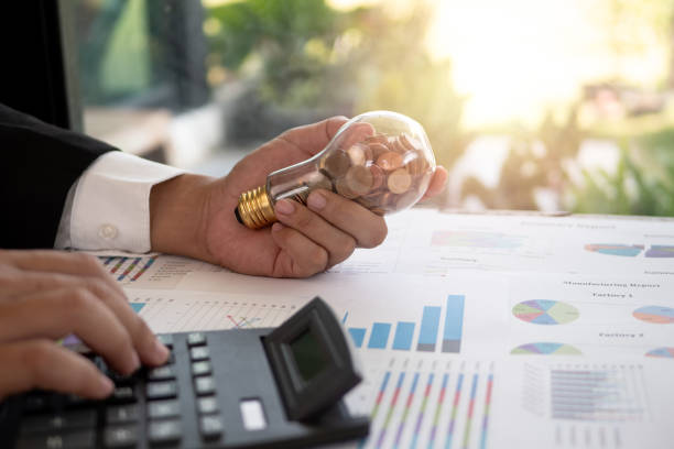 Hand of businessman hold light bulb with coin. Concept of Cost reduction and Reduce energy Hand of businessman hold light bulb with coin. Concept of Cost reduction and Reduce energy alternative energy stock pictures, royalty-free photos & images