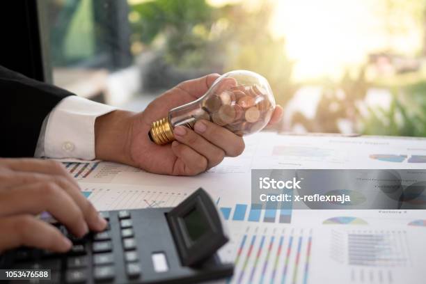 Hand Of Businessman Hold Light Bulb With Coin Concept Of Cost Reduction And Reduce Energy Stock Photo - Download Image Now