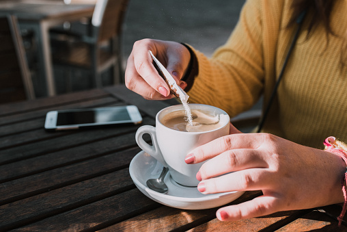 A woman pouring sugar in a latte coffee