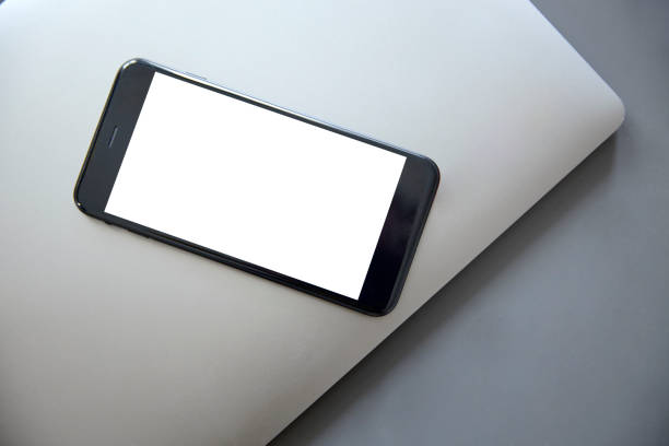 istock Smartphone with a white blank screen lies on a gray laptop 1053484932