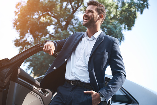 Un joven guapo con un traje sale el coche y risas photo