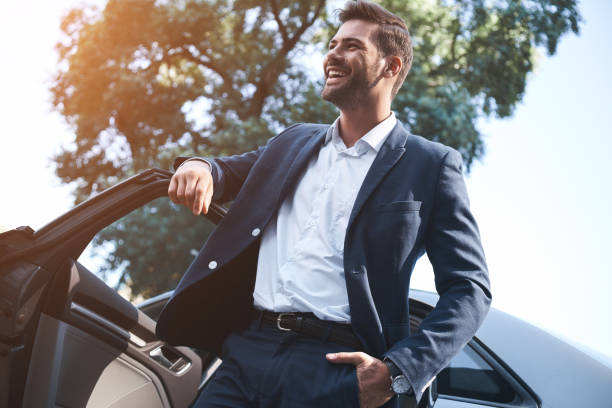 a young handsome man in a suit comes out of the car and laughs - businessman one man only standing elegance imagens e fotografias de stock