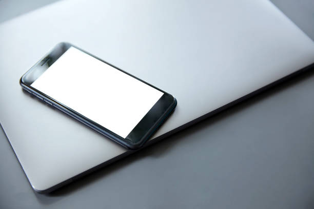 istock Smartphone with a white blank screen lies on a gray laptop 1053485178