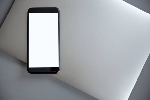 istock Smartphone with a white blank screen lies on a gray laptop 1053485262