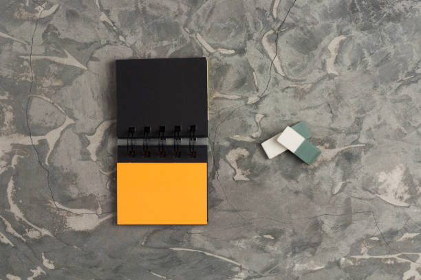 istock One blank paper notebook and two erasers on gray scratched  concrete table. Top view. Business or education concept 1053488744