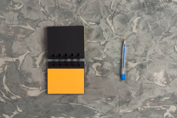 istock Blue pen and blank paper notebook on gray scratched concrete table. Top view. Business or education concept 1053488784