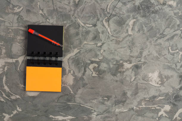 istock Red pen and blank paper notebook on gray scratched concrete table with copy space. Top view. Business or education concept 1053488846