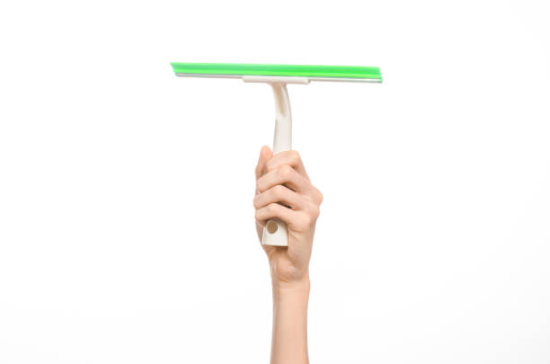 istock Household cleaning and washing windows theme: man's hand holding a green scraper windows isolated on a white background in the studio. 1053490754