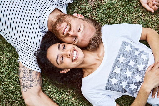 Portrait of happy man and woman relaxing in back yard. Directly above view of smiling multi-ethnic couple is lying on grass. They are in casuals.