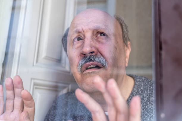 istock Old senior man looking throughout the window feeling confused and depressed alone at home in Aging Retirement Widower Dementia and Alzheimer concept. 1053516132