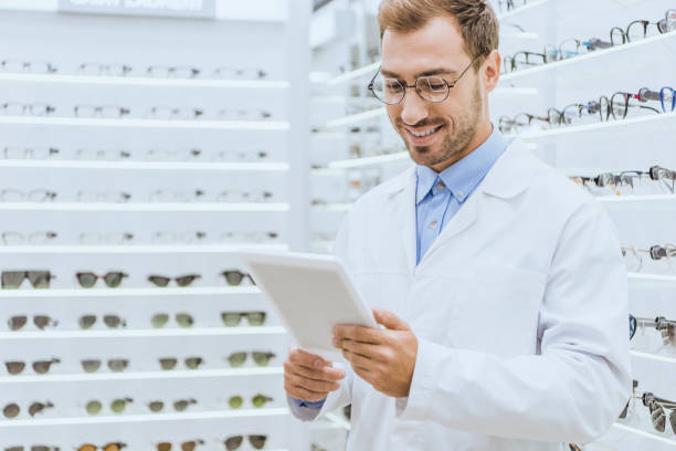 istock smiling male optician using digital tablet in optica with eyeglasses on shelves 1053516144